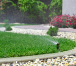 Sprinkler system head watering lawn with garden in the background | Pearson Sprinkler Co.